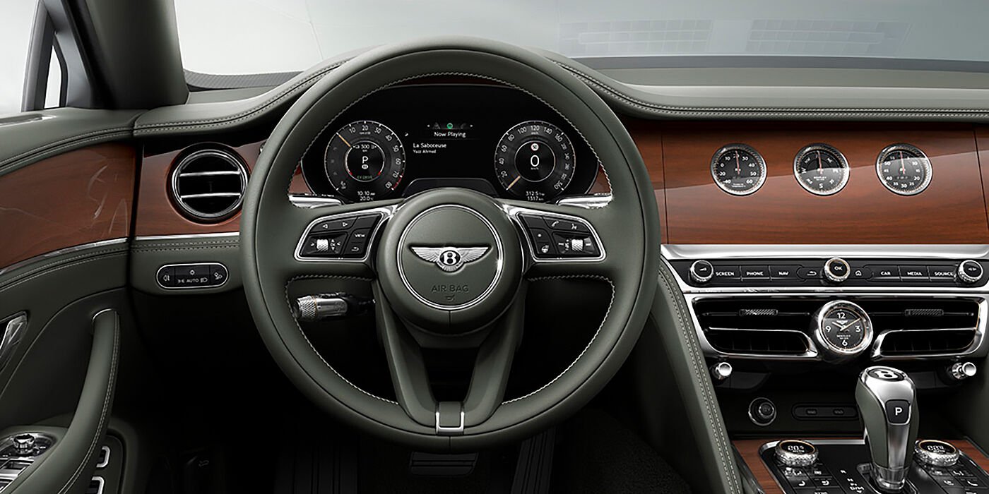 Bentley Auckland New Bentley Flying Spur sedan front cabin in Cumbrian Green hide and Crown Cut walnut veneer showing steering wheel and Rotating Display with three clocks on face