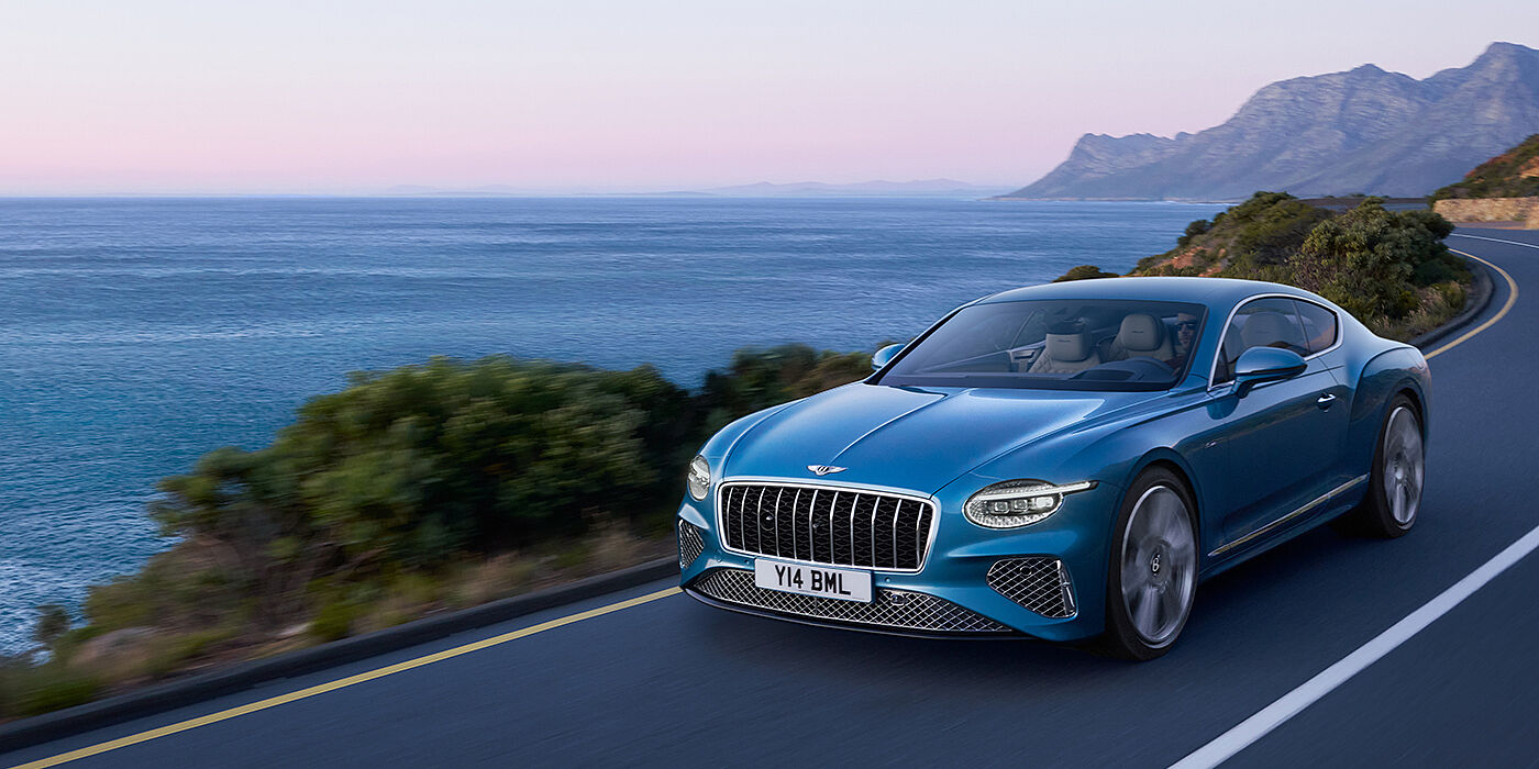 Bentley Auckland New Bentley Continental GT Azure coupe in Light Windsor blue paint with 22 inch Azure wheels and chrome grill, driving dynamically by the sea