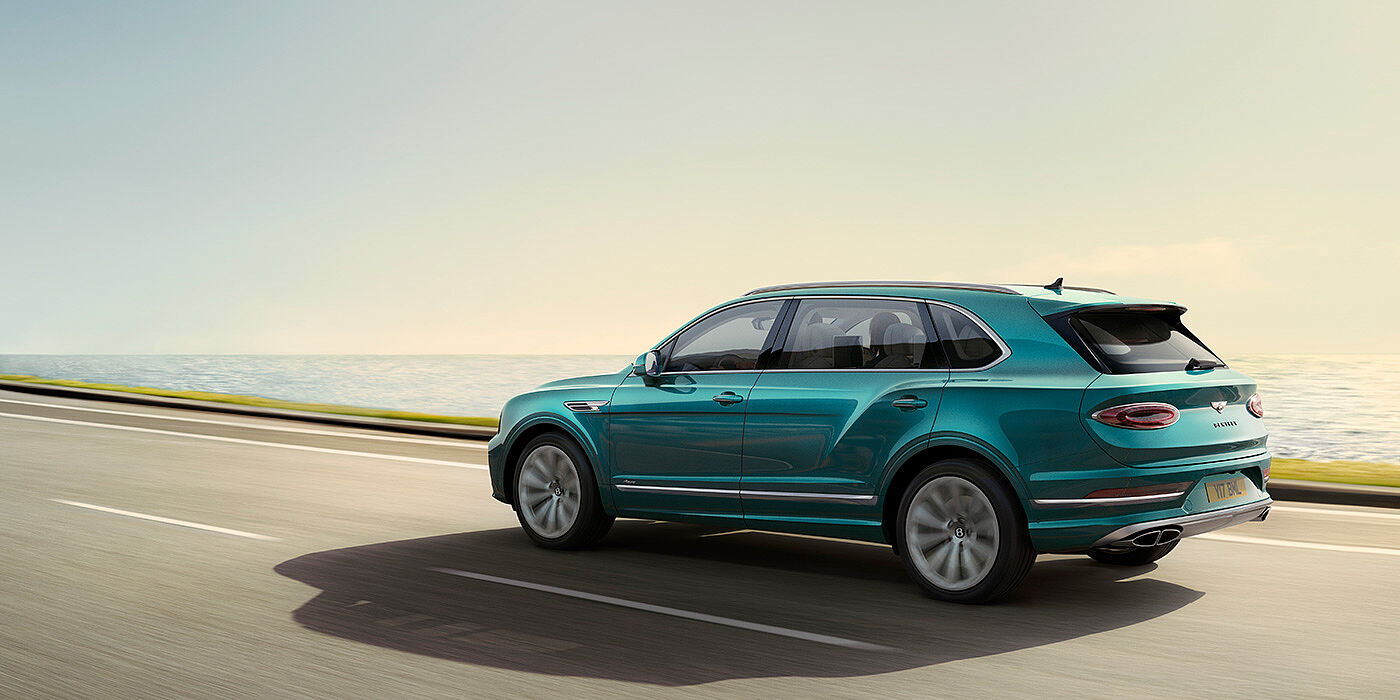 Bentley Auckland Rear view of a Topaz blue Bentley Bentayga EWB Azure, cruising along a sea side road.