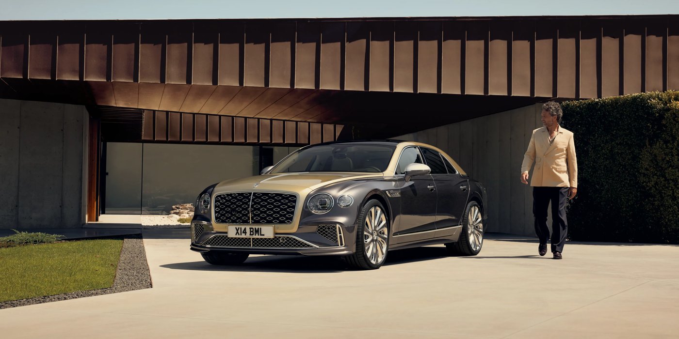 Bentley Auckland Bentley New Flying Spur Mulliner V8 hybrid sedan front three quarters in Rose Gold over Magnetic paint, parked near modern home