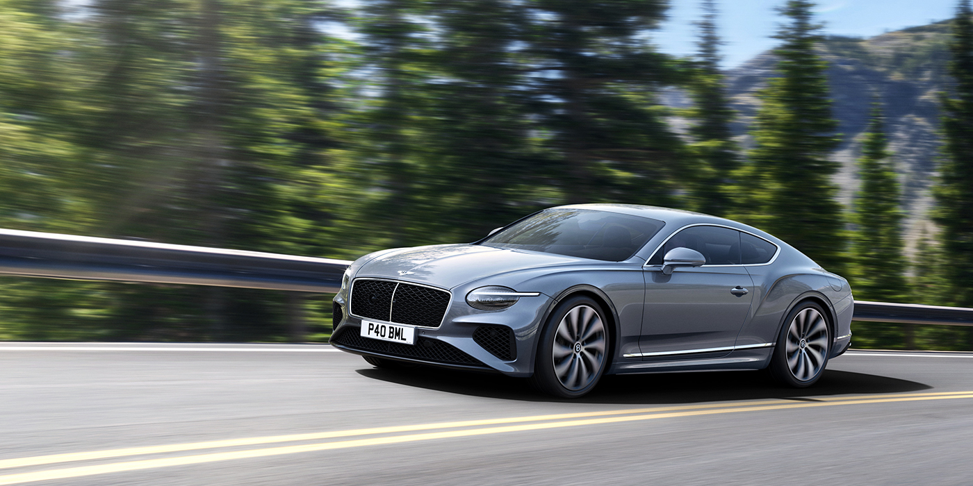 Bentley Auckland New Bentley Continental GT coupe in Silverlake paint and 22 inch ten-spoke wheels, driving dynamically on a tree-lined road in the sunshine