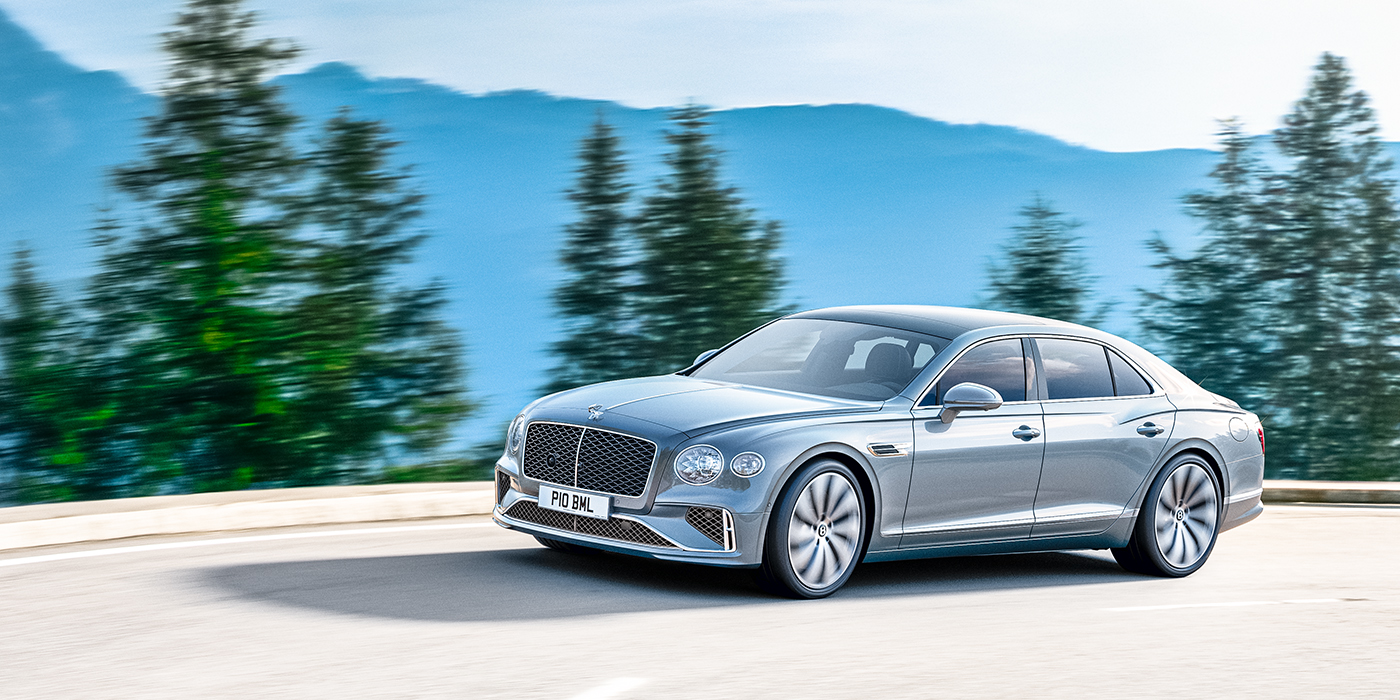 Bentley Auckland New Bentley Flying Spur sedan side view in Silverlake paint with ten spoke wheels and chrome matrix grille driving dynamically on a mountain road