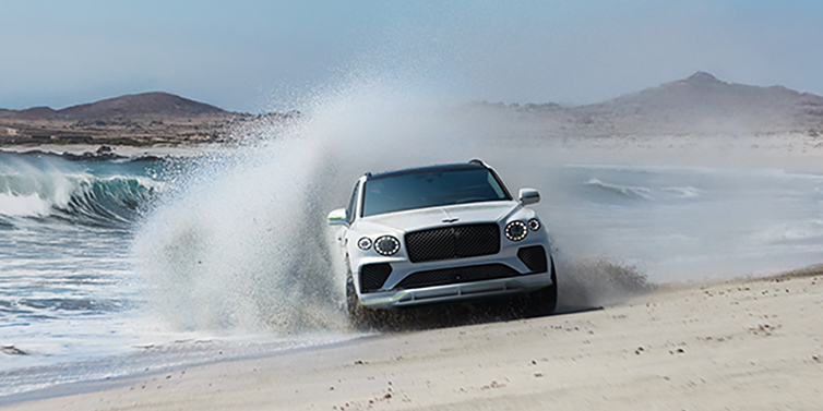 Bentley Auckland Bentley Bentayga Speed SUV facing front in Snow Quarts Pearlescent white paint driving dynamically on beach