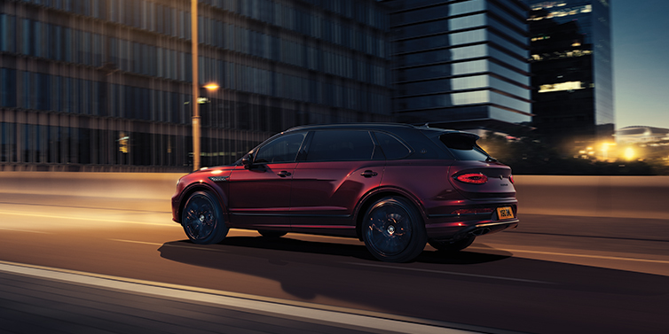 Bentley Auckland Bentley Bentayga Extended Wheelbase Mulliner SUV in Cricket Ball red paint driving dynamically in city at night
